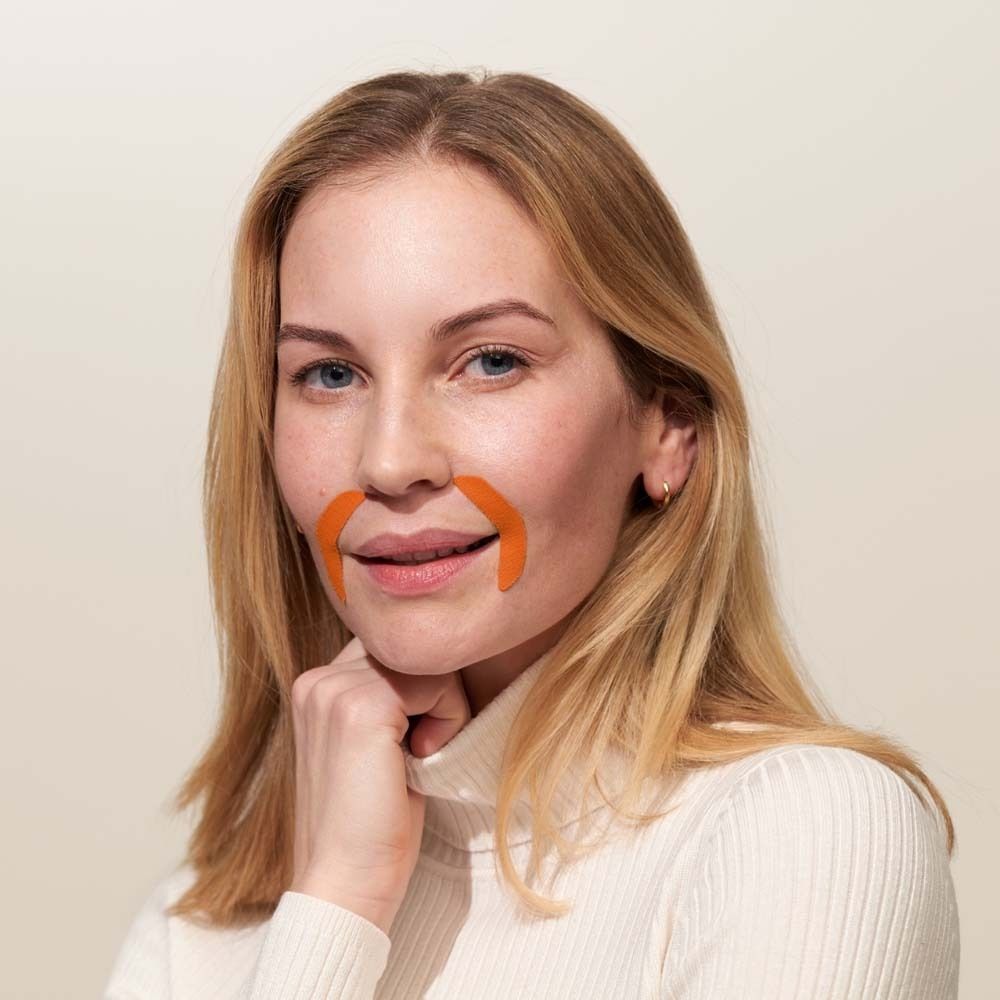 Frau mit orangefarbenen Mund-Patches. Sie trägt einen Rollkragenpullover.