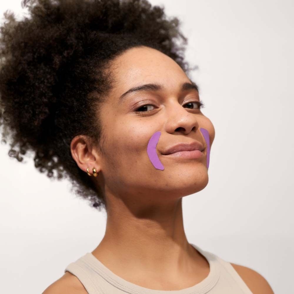 Frau mit zwei lila Mund Patches auf den Wangen. Sie lächelt.