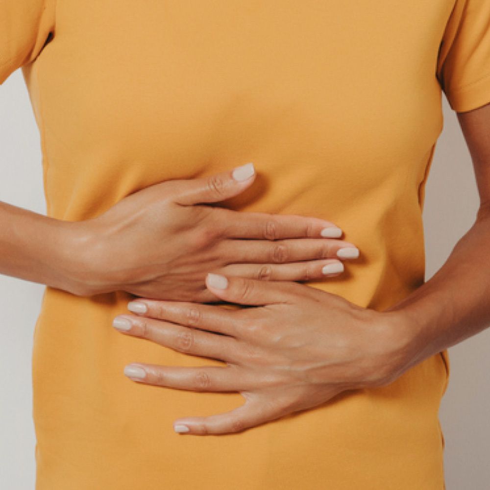 Person hält Hände auf Bauch. Gelbes T-Shirt. Fokus auf den Bauchbereich.