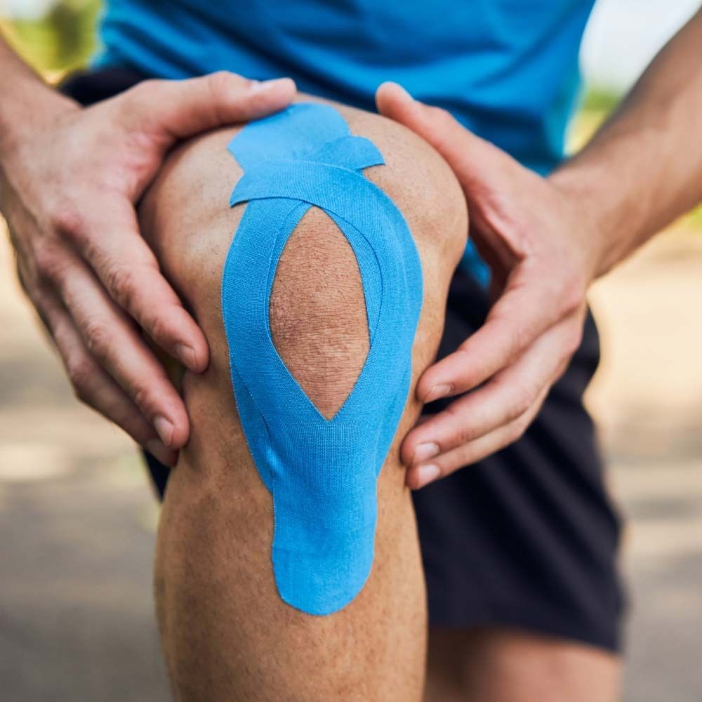 Knie mit blauem Kinesiologie Tape. Das Tape ist überlappend angebracht.