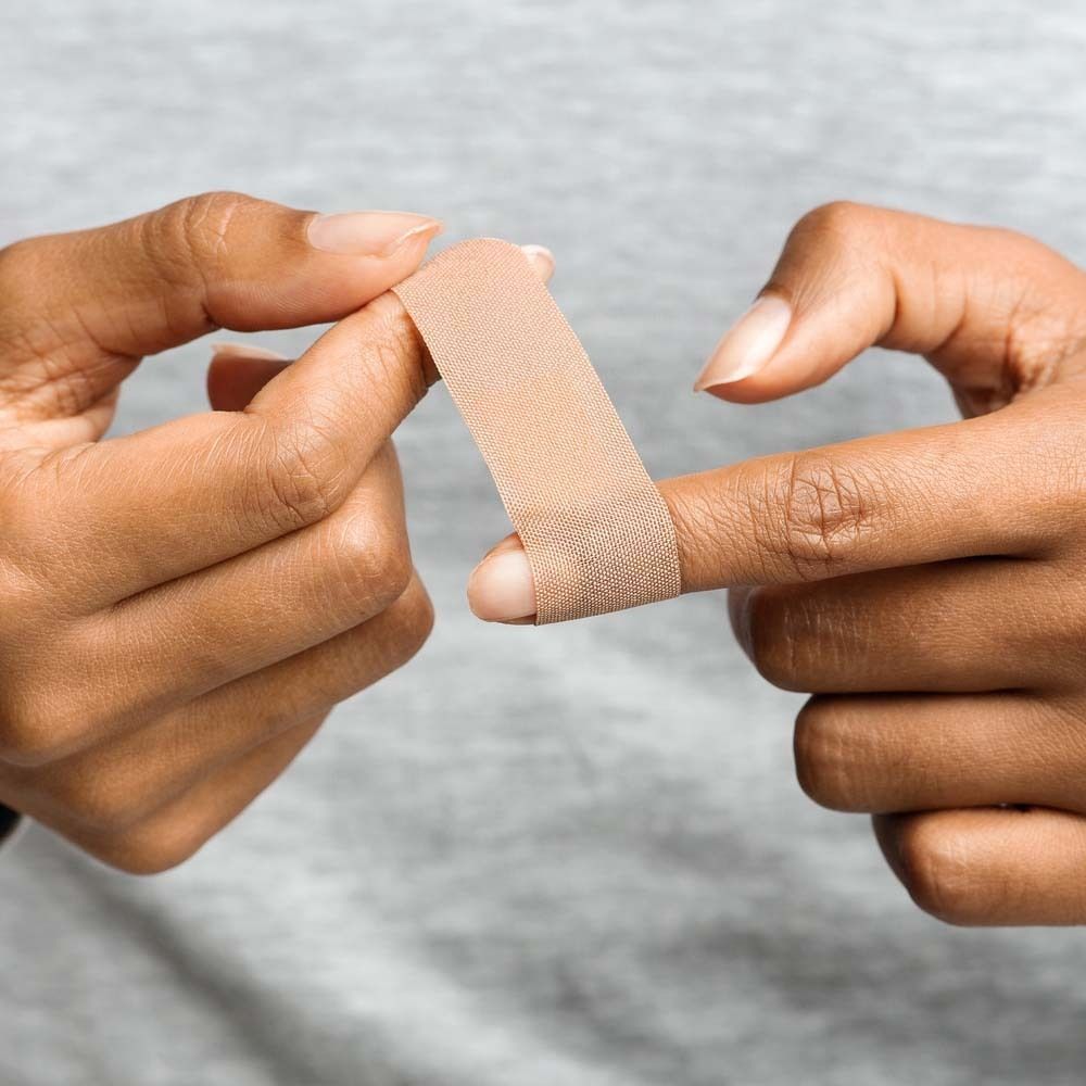 Hände kleben Fingerpflaster. Beige Pflaster auf Finger. Grauer Hintergrund.