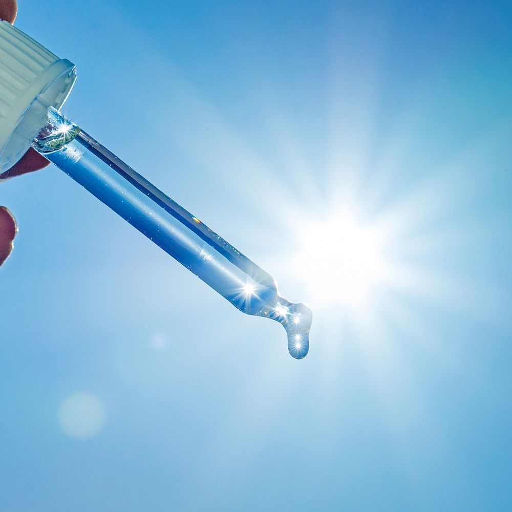 Blaue Pipette mit Tropfen vor sonnigem Hintergrund. Flüssigkeit tropft aus der Pipette.