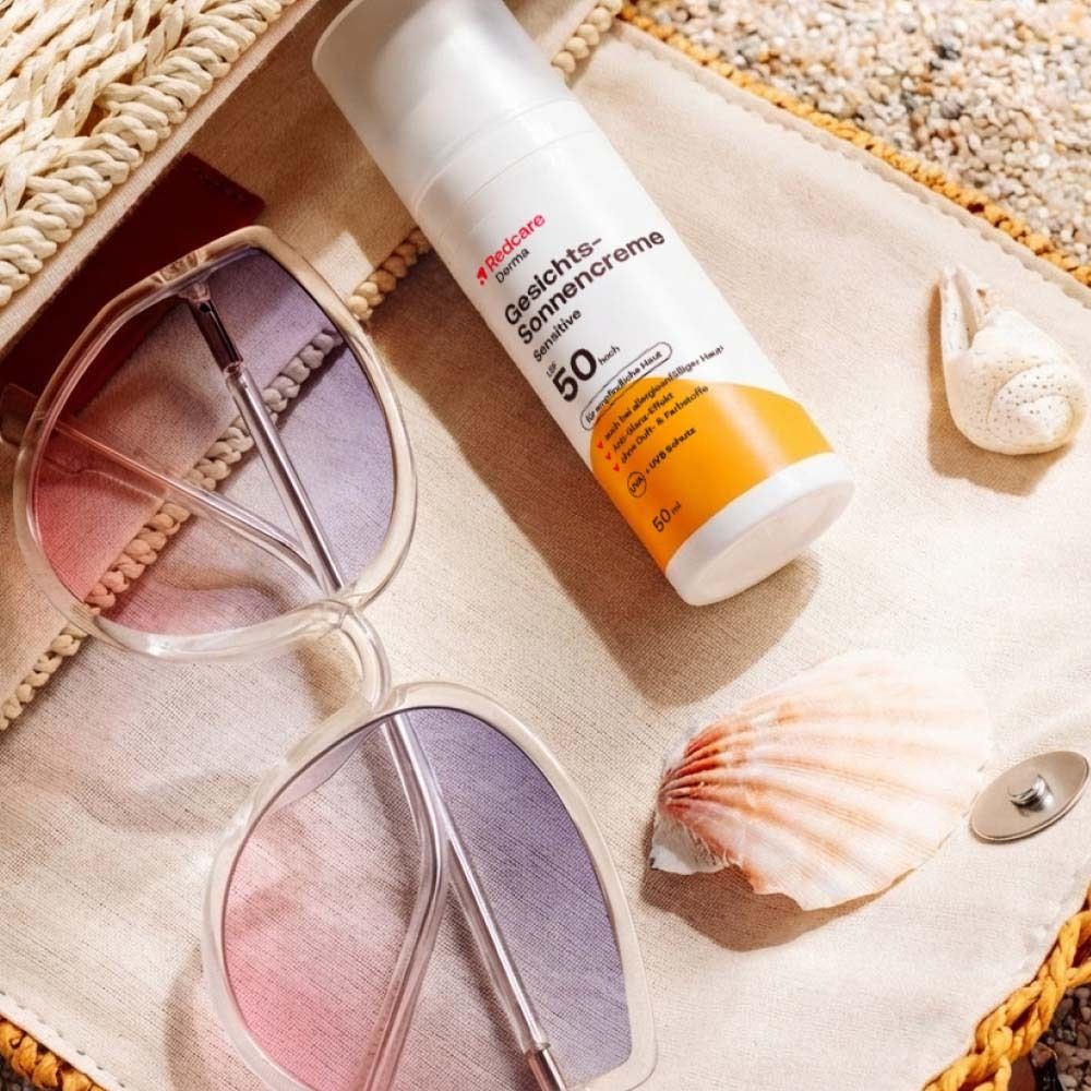 Sonnencreme-Flasche, Sonnenbrille und Muschel auf einer Strandtasche. Strandhintergrund.