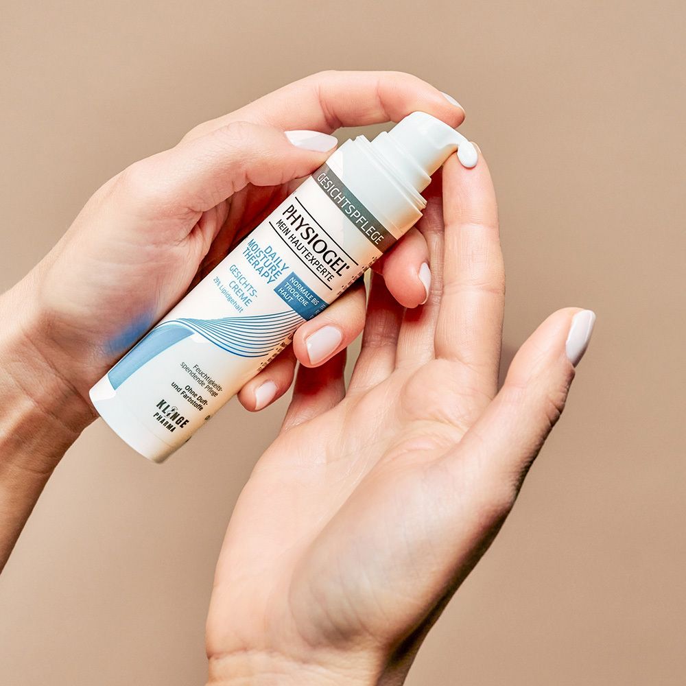 Hände halten Tube PHYSIOGEL Daily Moisture Therapy Gesichtscreme. Creme wird ausgedrückt.