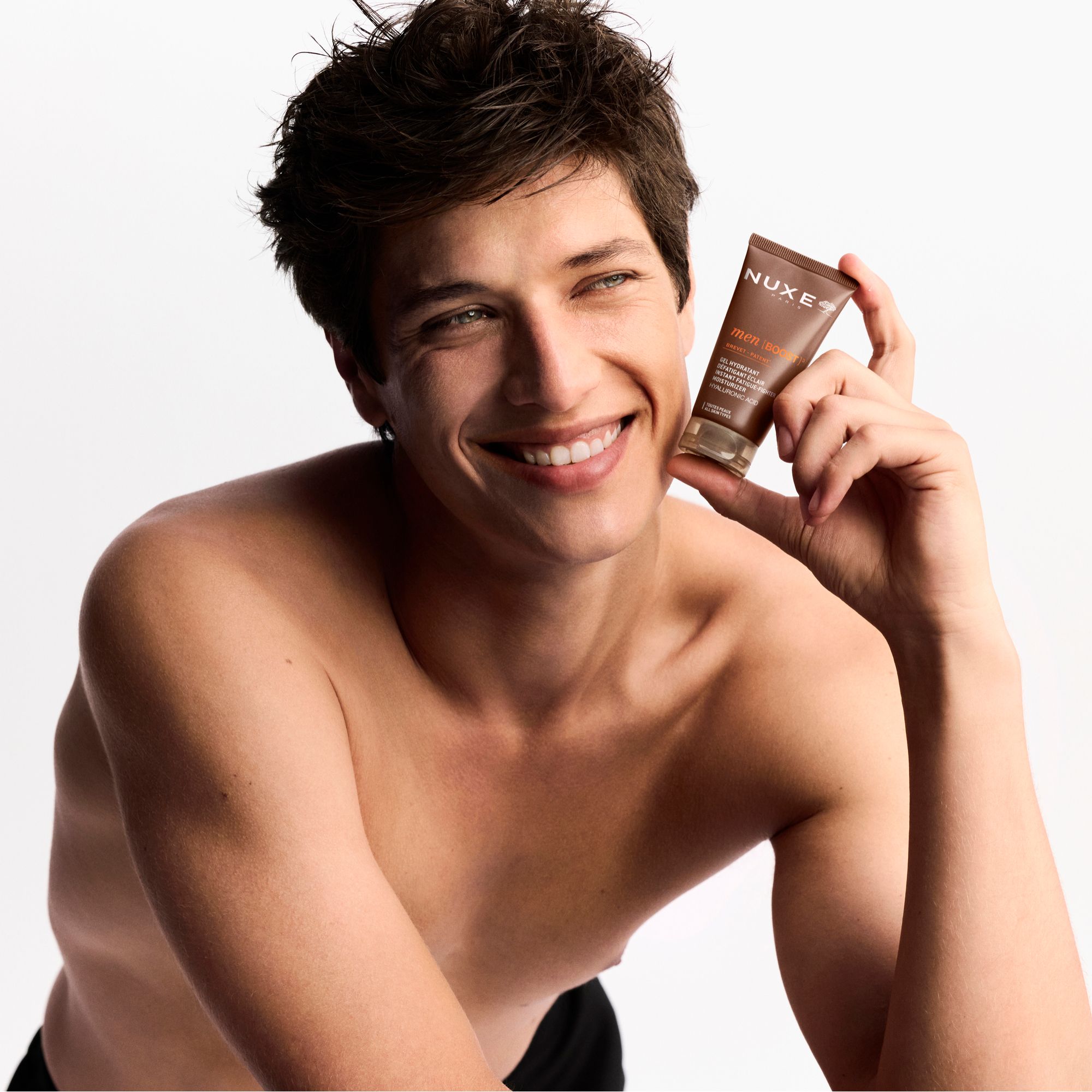 Mann hält Tube men [BOOST]³ in der Hand. Lächelt. Oben ohne. Produktverpackung sichtbar.