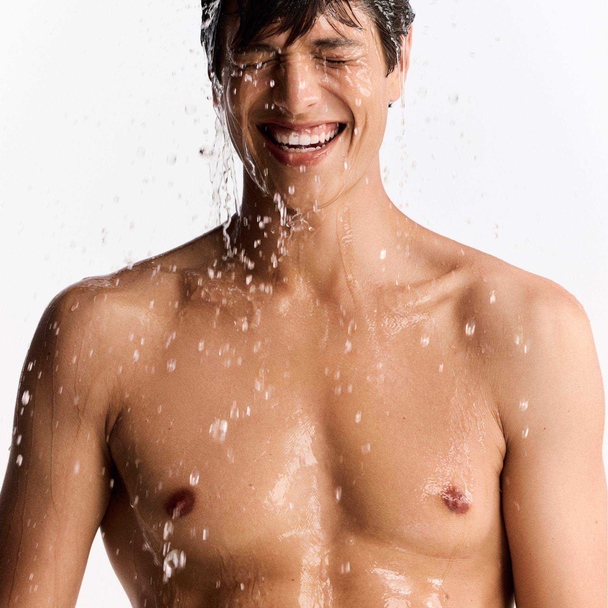 Mann mit Wasser im Gesicht. Wasser spritzt. Gesichtsausdruck: Lächeln.