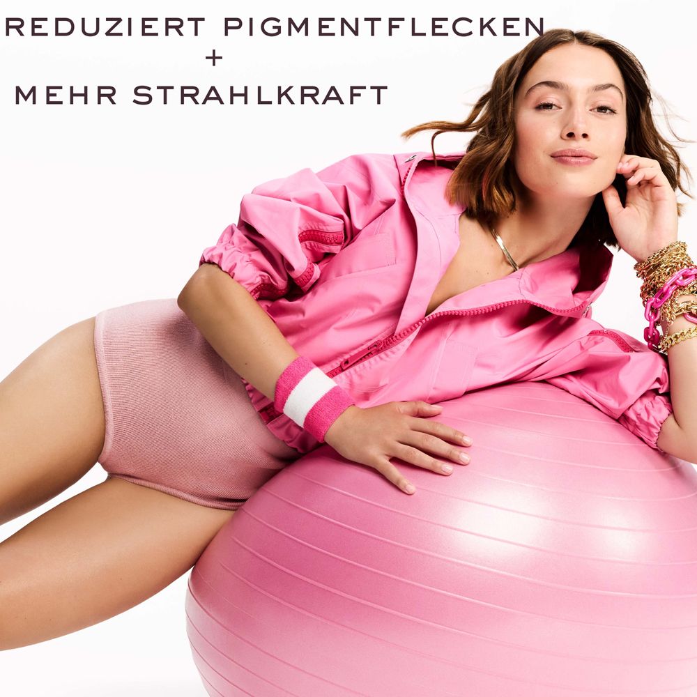 Frau auf einem rosa Gymnastikball. Text: REDUZIERT PIGMENTFLECKEN + MEHR STRAHLKRAFT. Sie trägt rosa Kleidung.