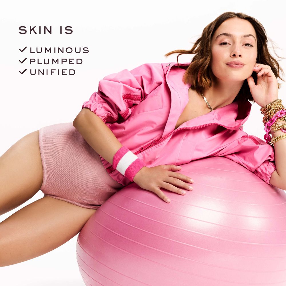 Frau liegt auf einem rosa Gymnastikball. Sie trägt rosa Sportkleidung. Text: SKIN IS, Luminous, Plumped, Unified.