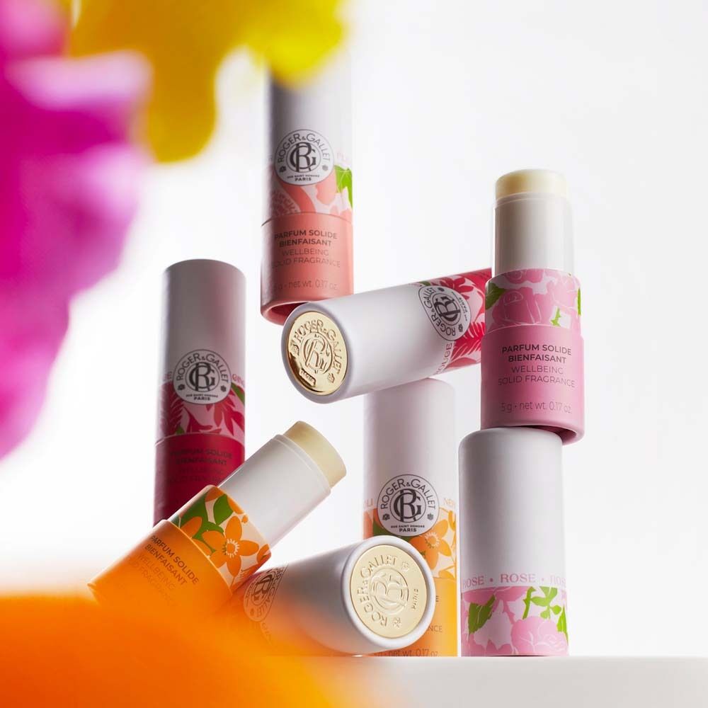 Mehrere zylindrische Behälter. Rosa und orangefarbene Verpackung. Text: Parfum Solide Bienfaisant.