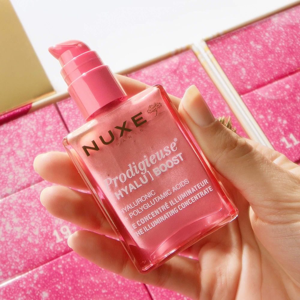 Eine Hand hält eine Flasche Nuxe Prodigieuse Hyalu [Boost] Illuminating Concentrate.