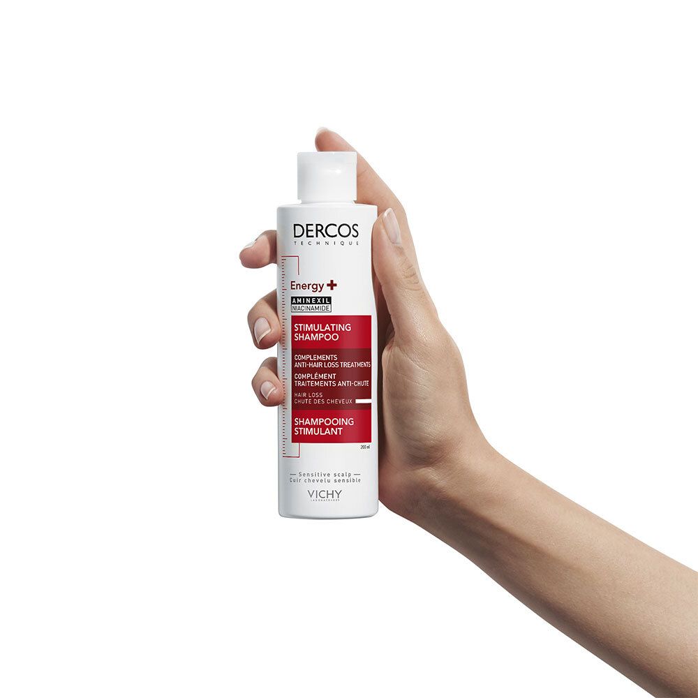 Hand hält Shampoo. Weiß mit roter Beschriftung. Marke Dercos, Energy+, Aminexil.