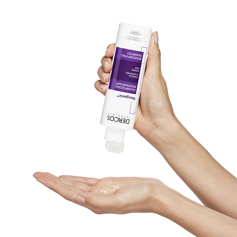 Mains tenant un flacon de shampooing. Le produit est versé dans la paume. Liquide blanc.