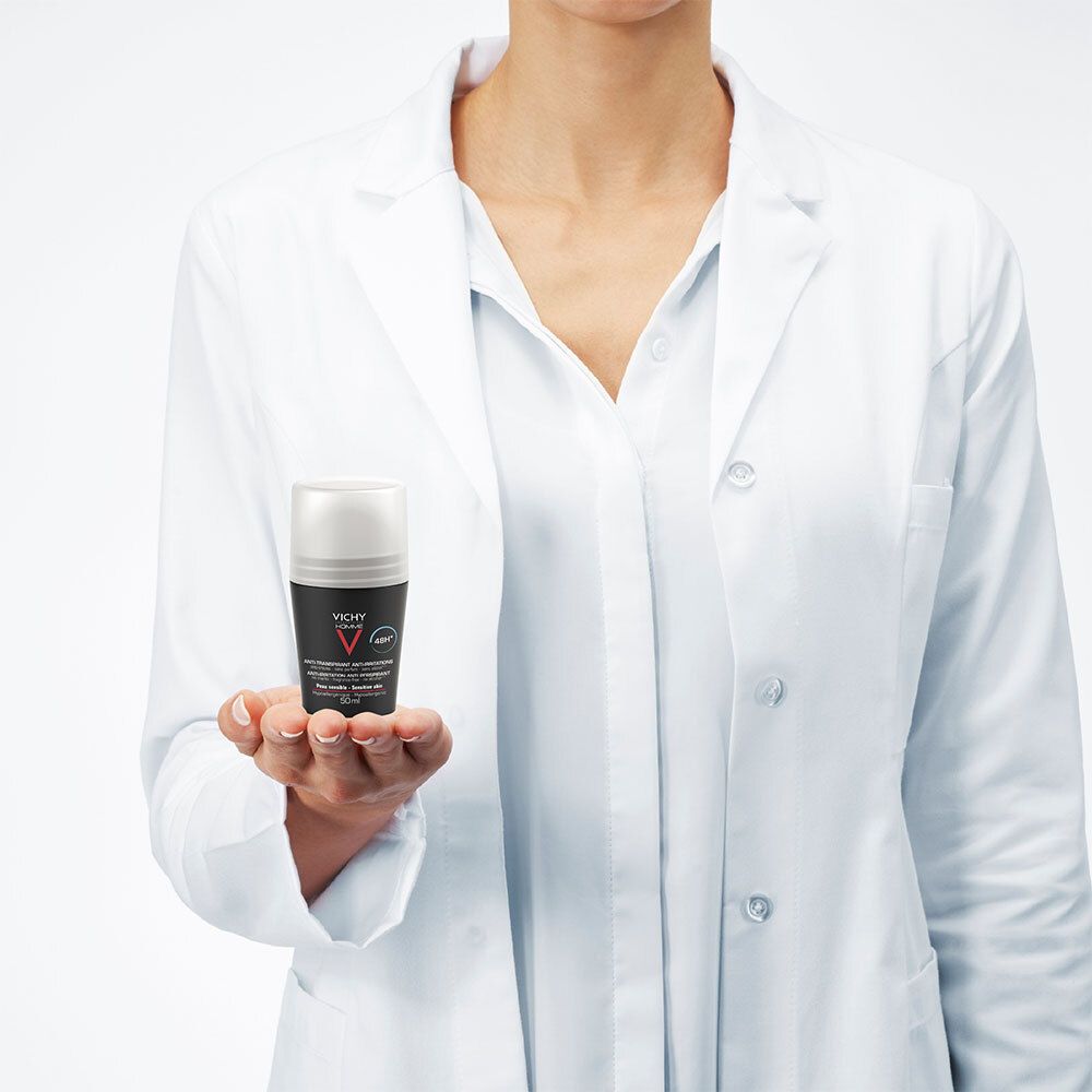 Eine Person in einem weißen Laborkittel hält einen Deodorant-Roll-on. Schwarze Flasche, weißer Deckel. Marke: Vichy Homme.
