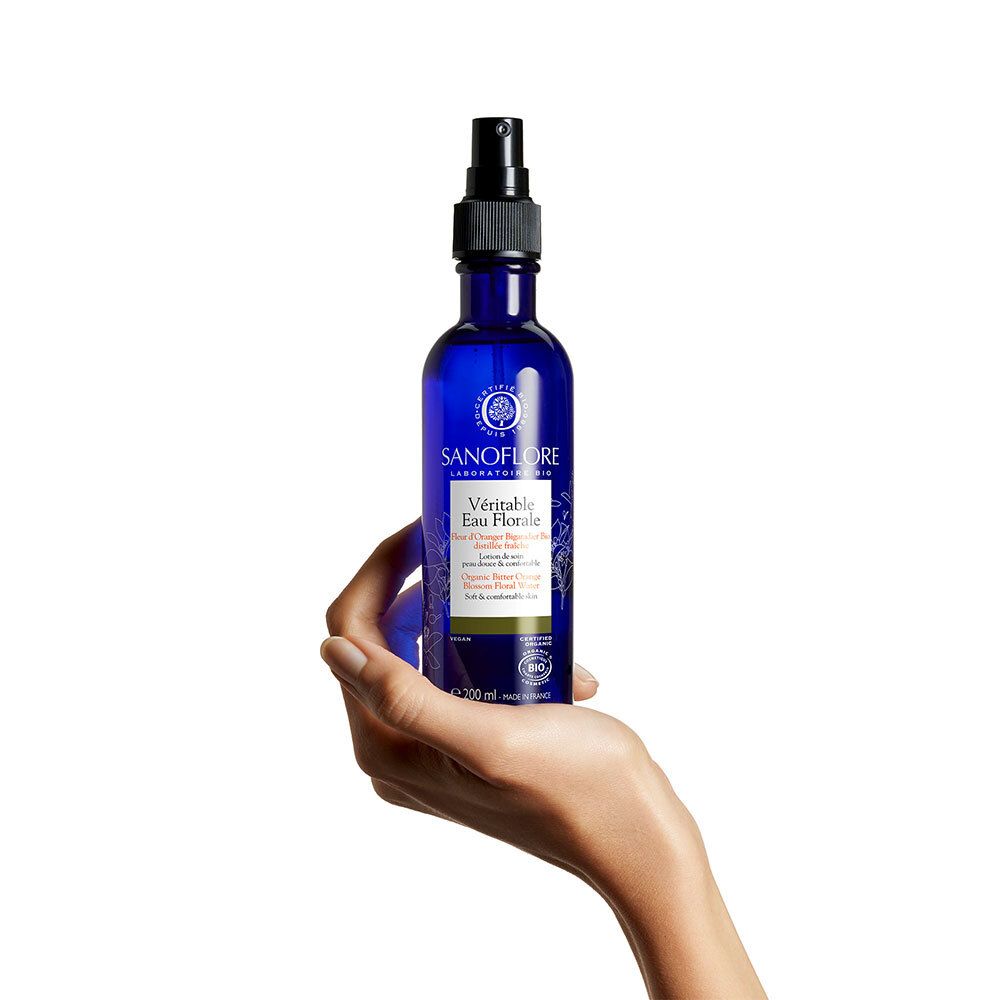 Flacon bleu avec vaporisateur tenu dans une main. Inscription: Sanoflore, Véritable Eau Florale.