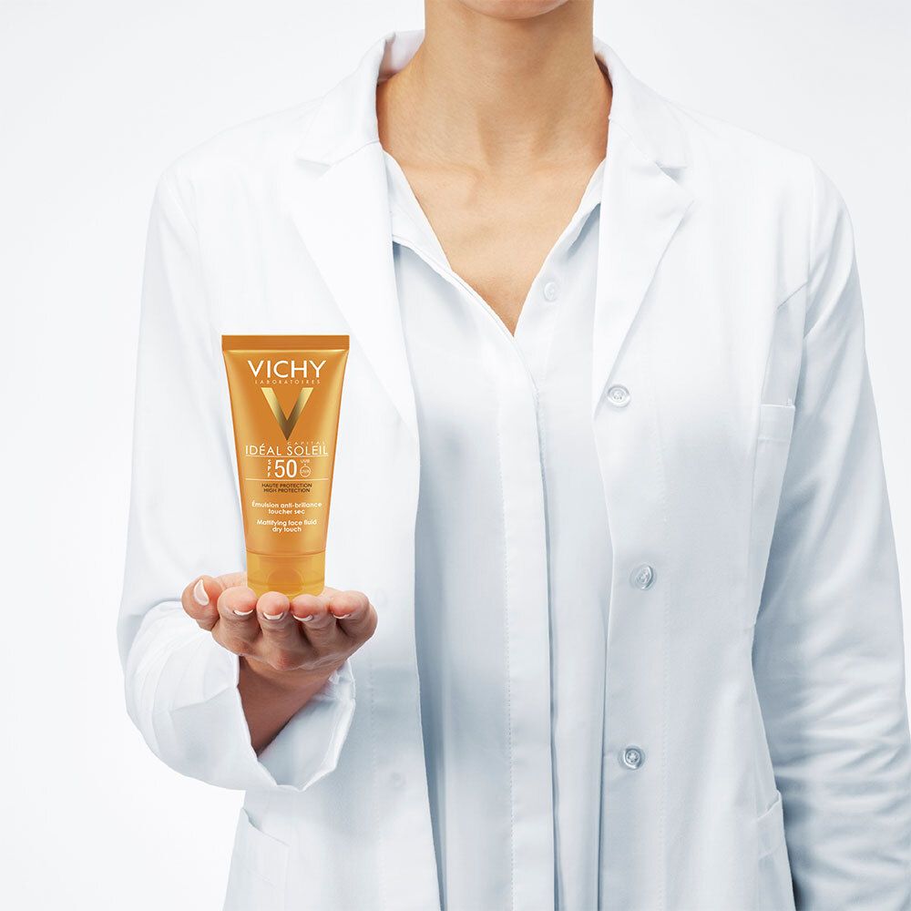 Personne tenant un tube Vichy Ideal Soleil SPF 50. La personne porte une blouse blanche. Produit en évidence.