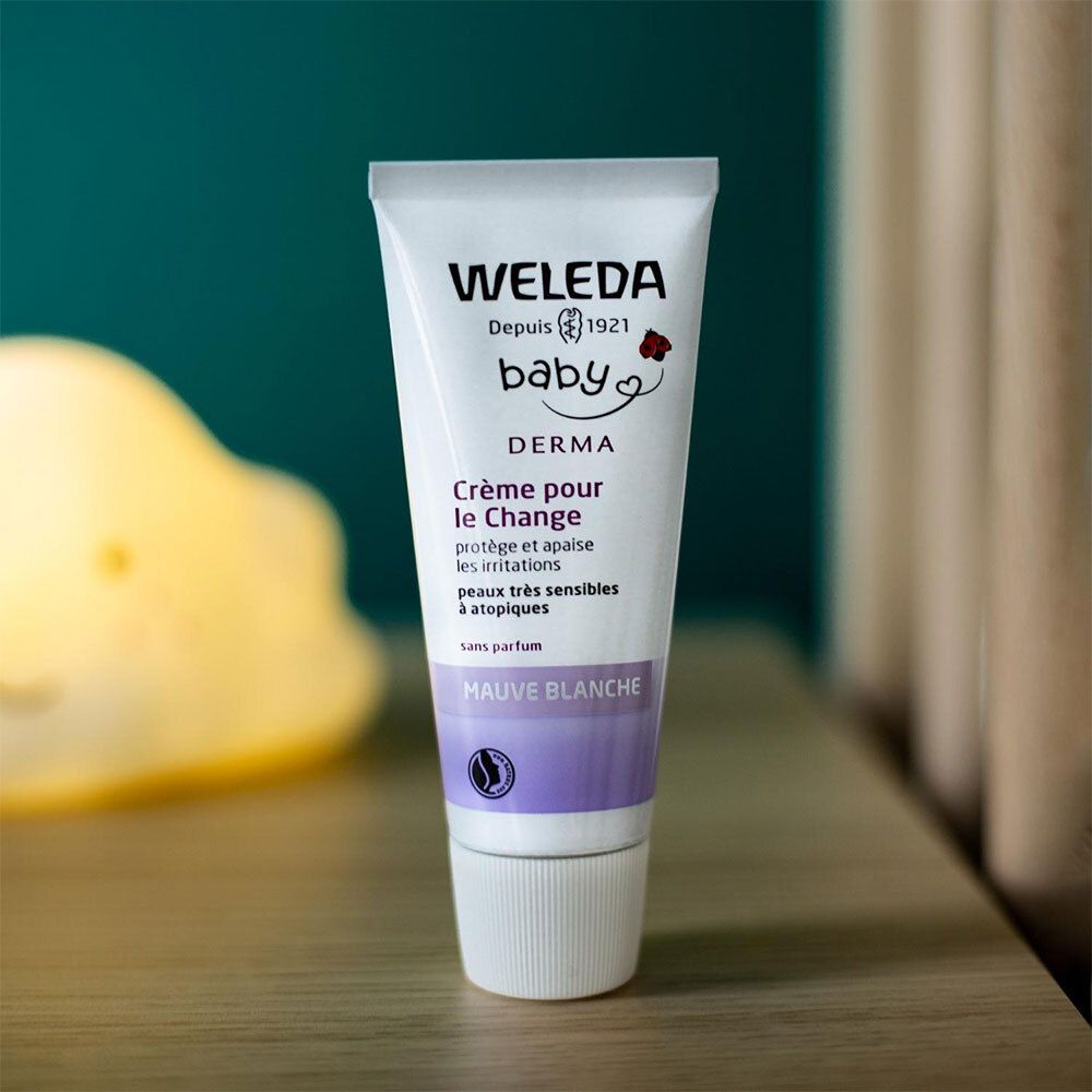Weleda Baby Derma Creme. Tube auf einem Tisch. Aufschrift: Crème pour le Change, schützt und beruhigt. Mit weißer Malve.