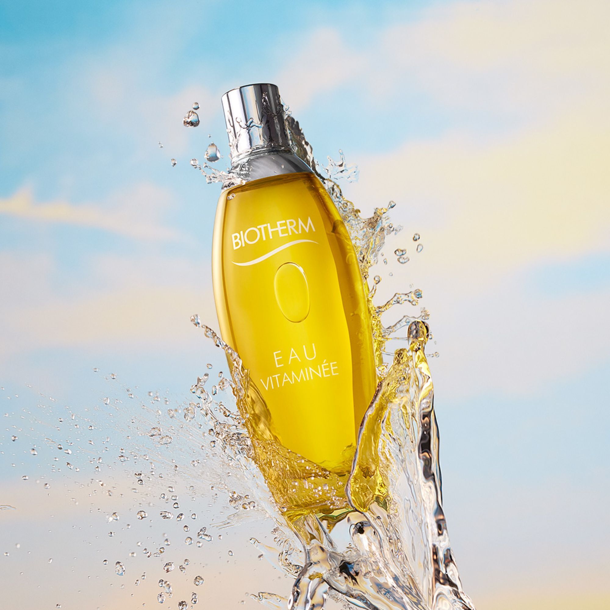 Flacon jaune dans l'eau. Inscription: Biotherm, EAU Vitaminée. Éclaboussures.