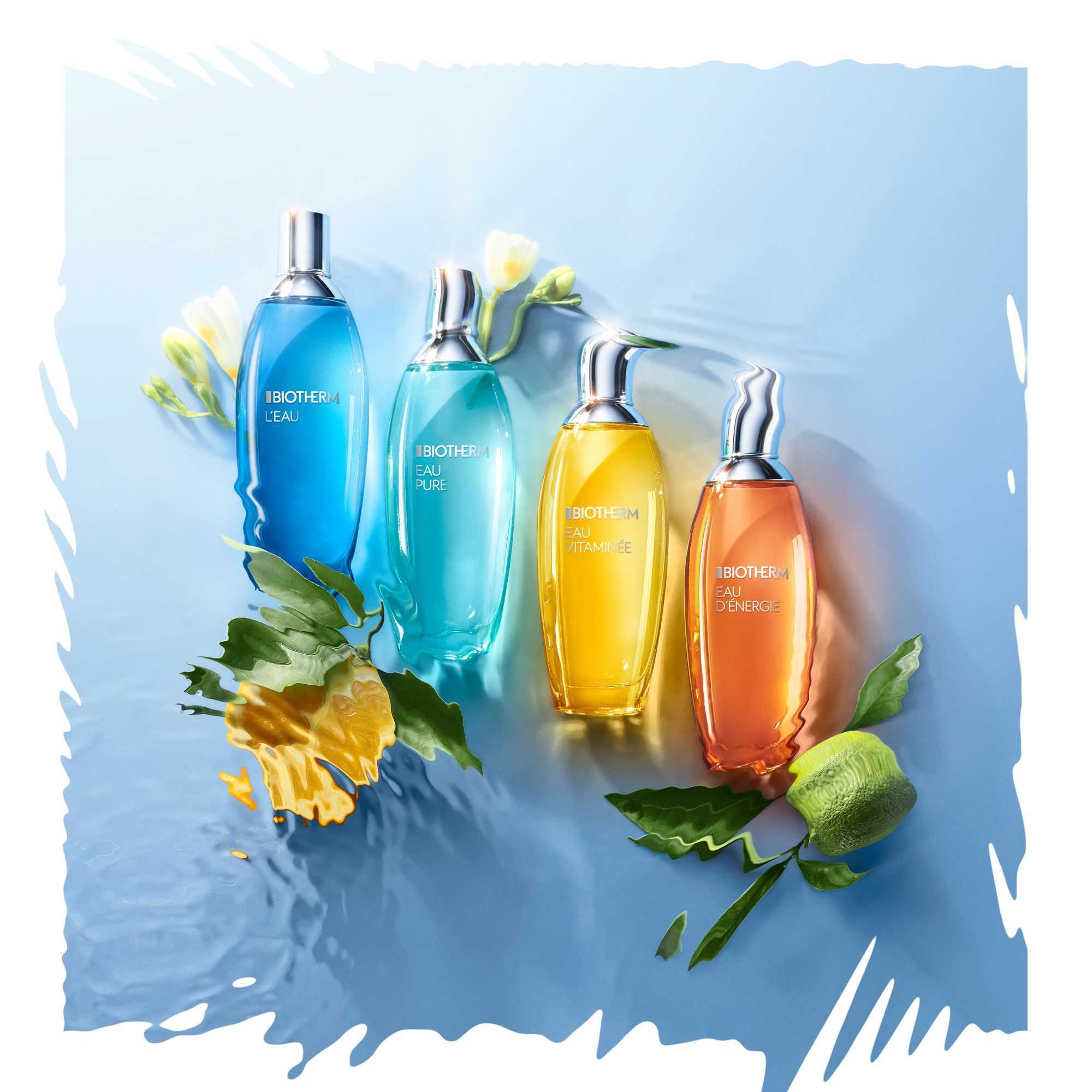 Vier BIOTHERM EAU PURE Körpersprays auf blauem Hintergrund. Unterschiedliche Farben. Dekoriert mit Früchten und Blättern.