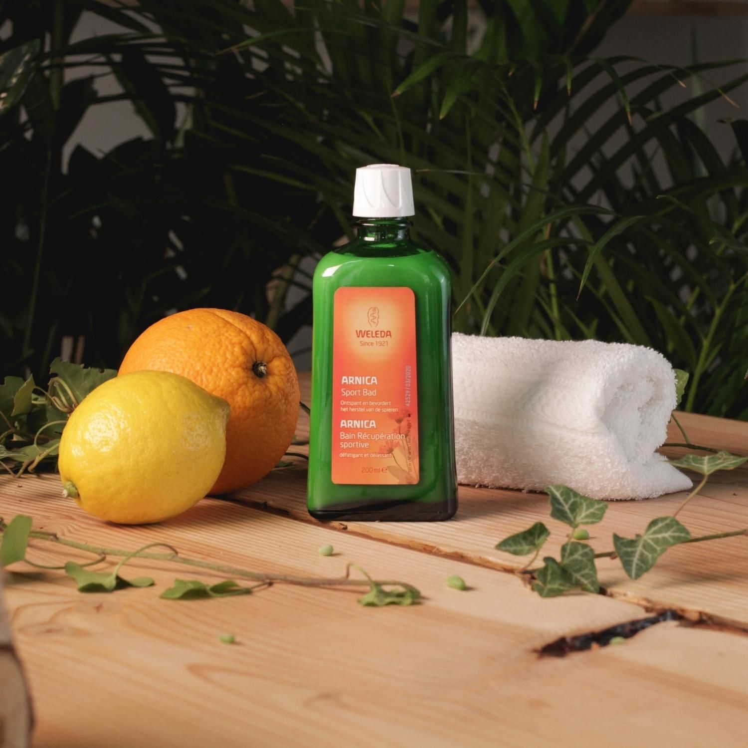 Bouteille verte avec bouchon blanc, à côté de citron, orange et serviette. Logo Weleda, nom Arnica.