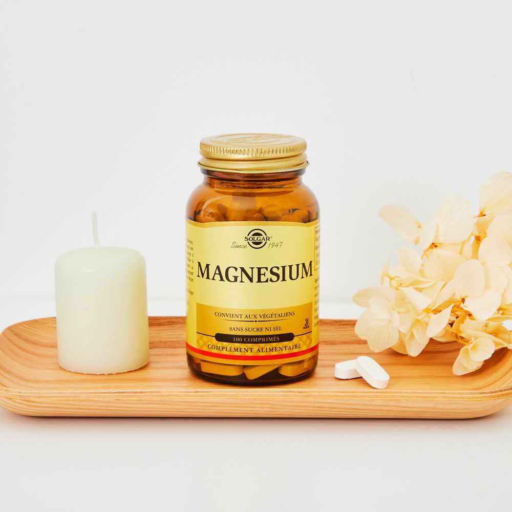 Flacon en verre brun avec couvercle doré et "SOLGAR Magnesium" sur un plateau en bois. À côté, une bougie et des fleurs.