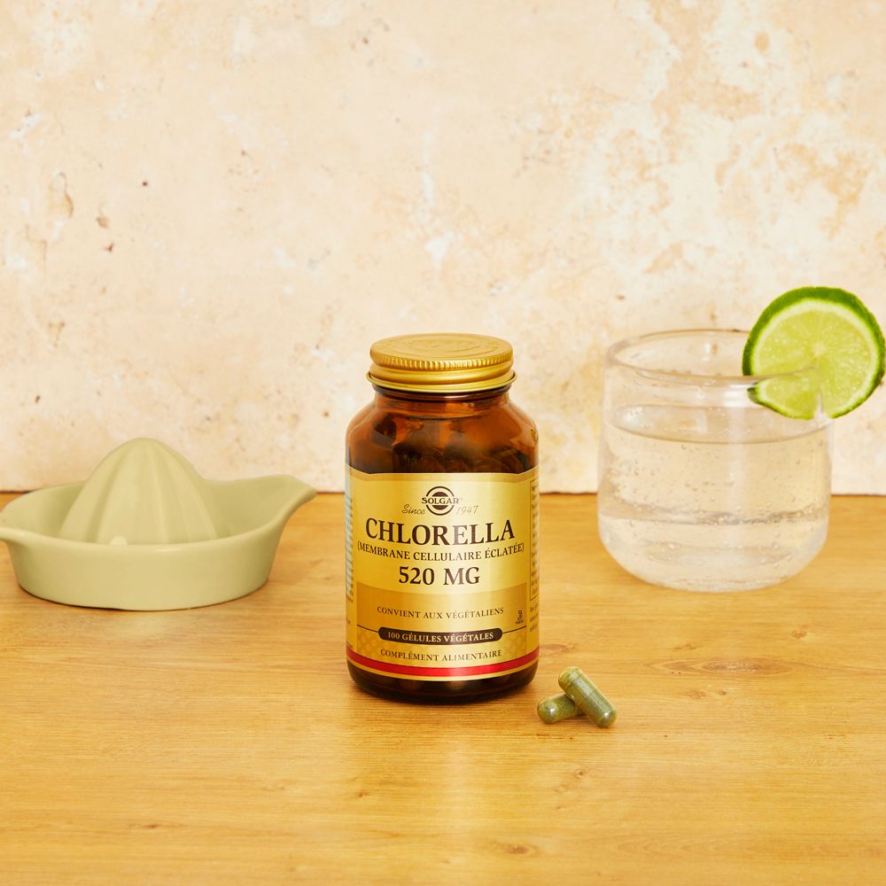 Flacon brun, bouchon doré, gélules Chlorella, verre d'eau et citron vert, presse-agrumes sur bois.