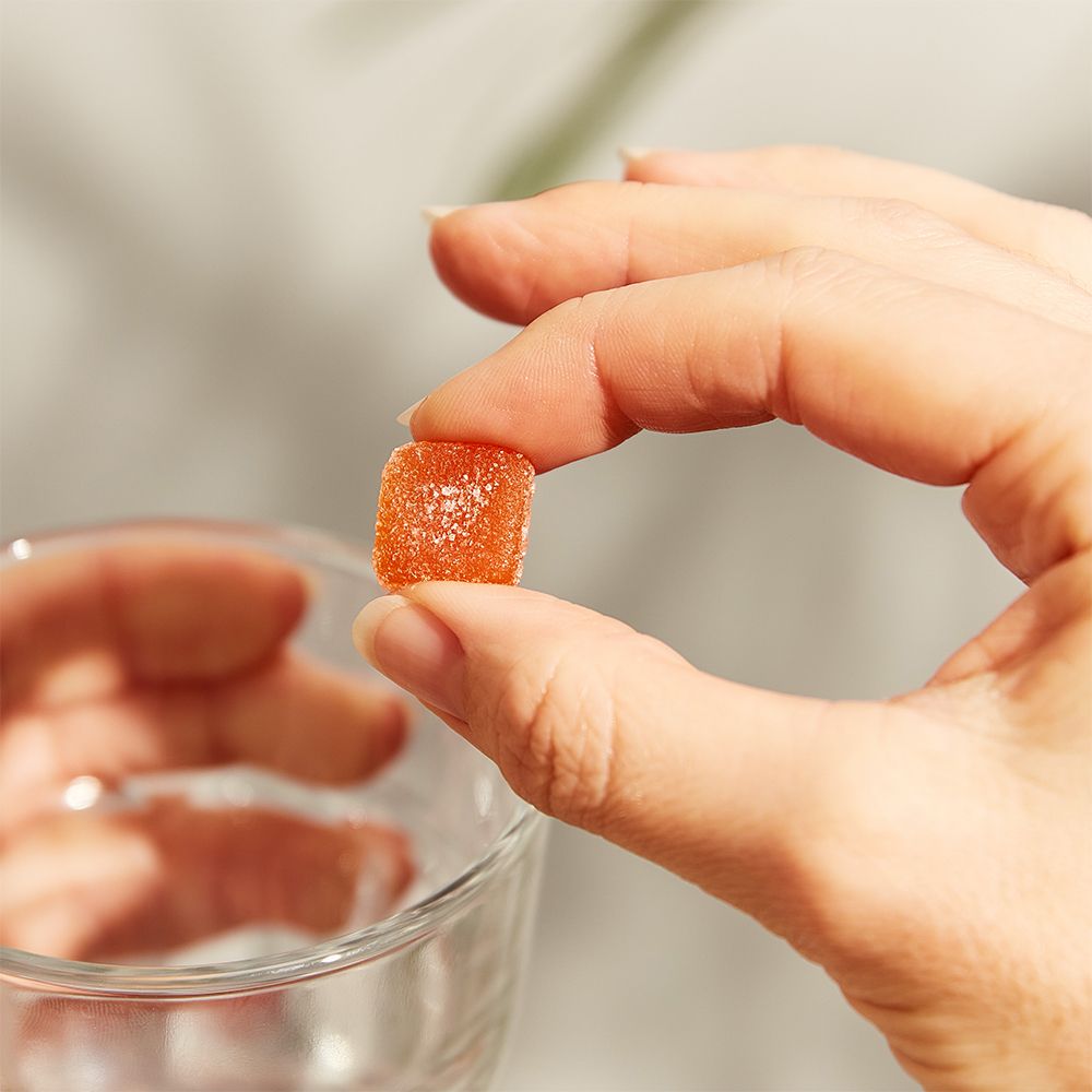 Main tenant un bonbon gélifié orange carré. Un verre en arrière-plan.