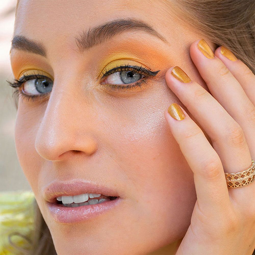 Nahaufnahme einer Frau mit gelbem Lidschatten und schwarzem Eyeliner. Goldener Ring am Finger.