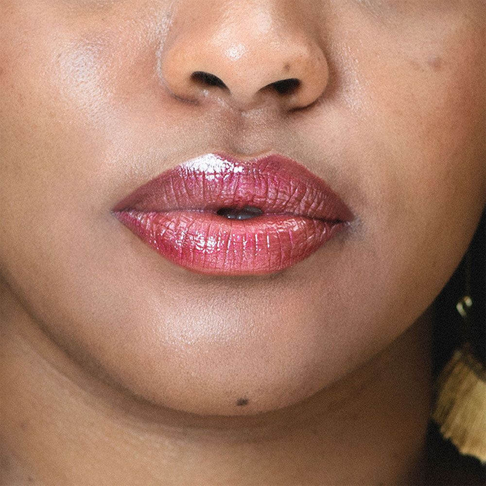 Nahaufnahme von Lippen, die mit einem rot-violetten Lippenstift bemalt sind. Die Lippen sind glänzend.