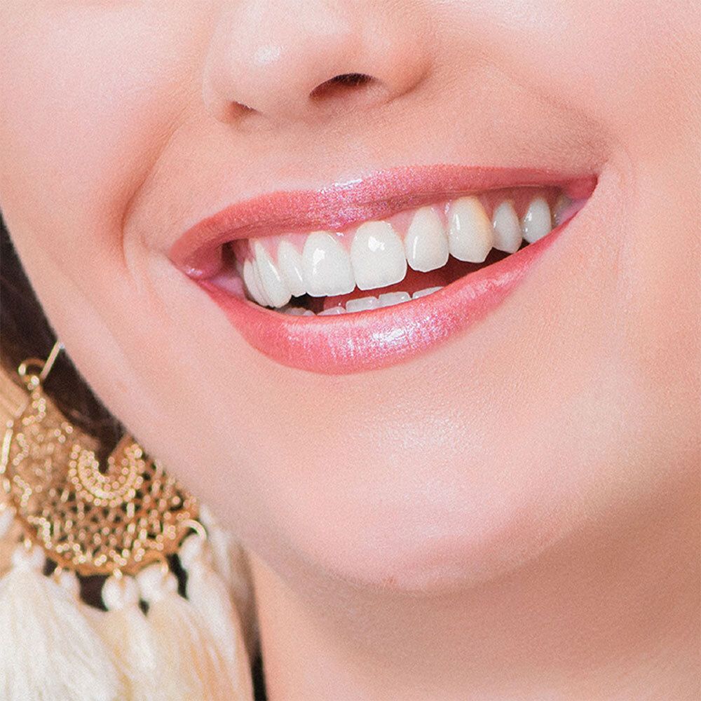 Nahaufnahme von Lippen mit rosafarbenem Lippenstift. Die Lippen sind leicht geöffnet, die Zähne sichtbar. Goldener Ohrschmuck.
