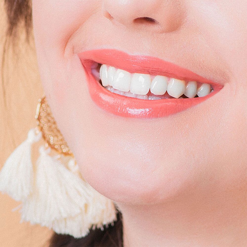 Nahaufnahme eines Lächelns mit rosafarbenem Lippenstift. Sichtbare Zähne und Lippen. Ohrring mit Quasten.