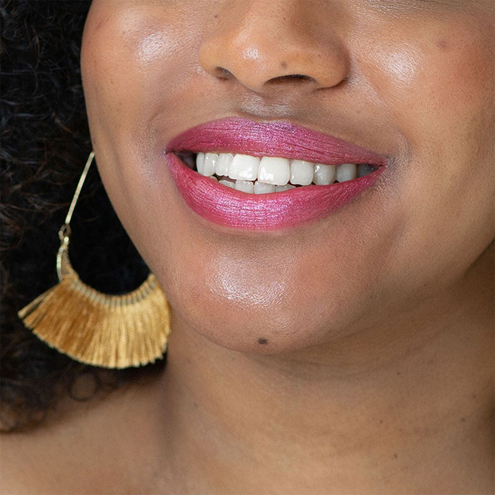 Nahaufnahme von Lippen mit rosa Lippenstift. Goldener Ohrring. Hautton. Gezahnte Zähne.