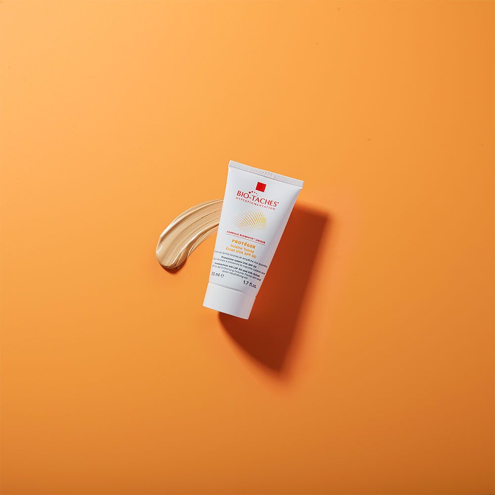 Tube BIO-TACHES® SOLAIRE LSF 50 et échantillon sur fond orange. Tube blanc et substance crémeuse.
