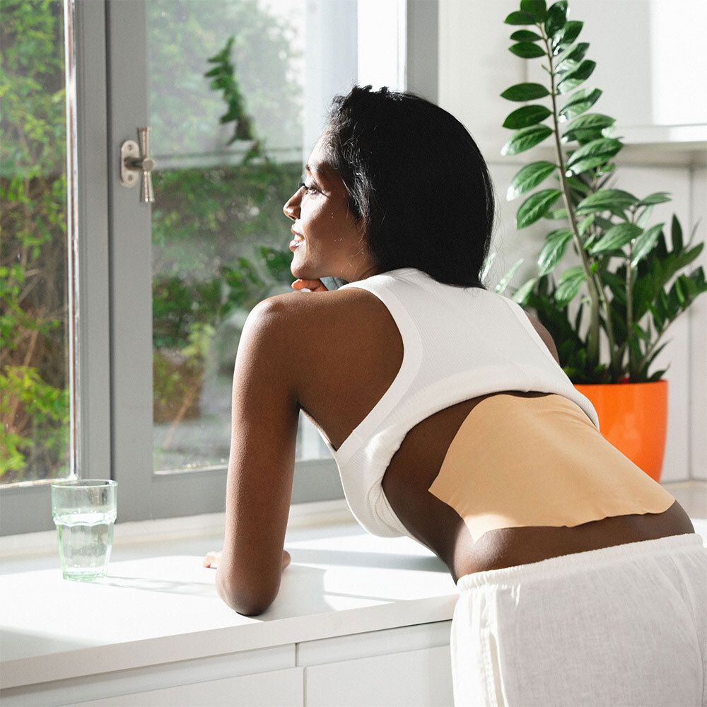 Dos d'une femme avec un patch chauffant. Beige, forme triangulaire.