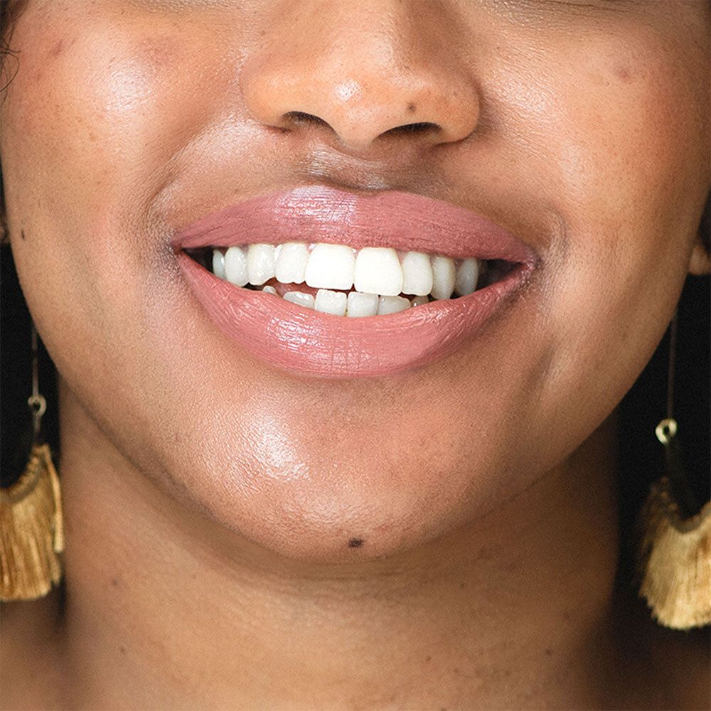 Nahaufnahme eines lächelnden Gesichts mit rosafarbenem Lippenstift. Goldene Ohrringe.