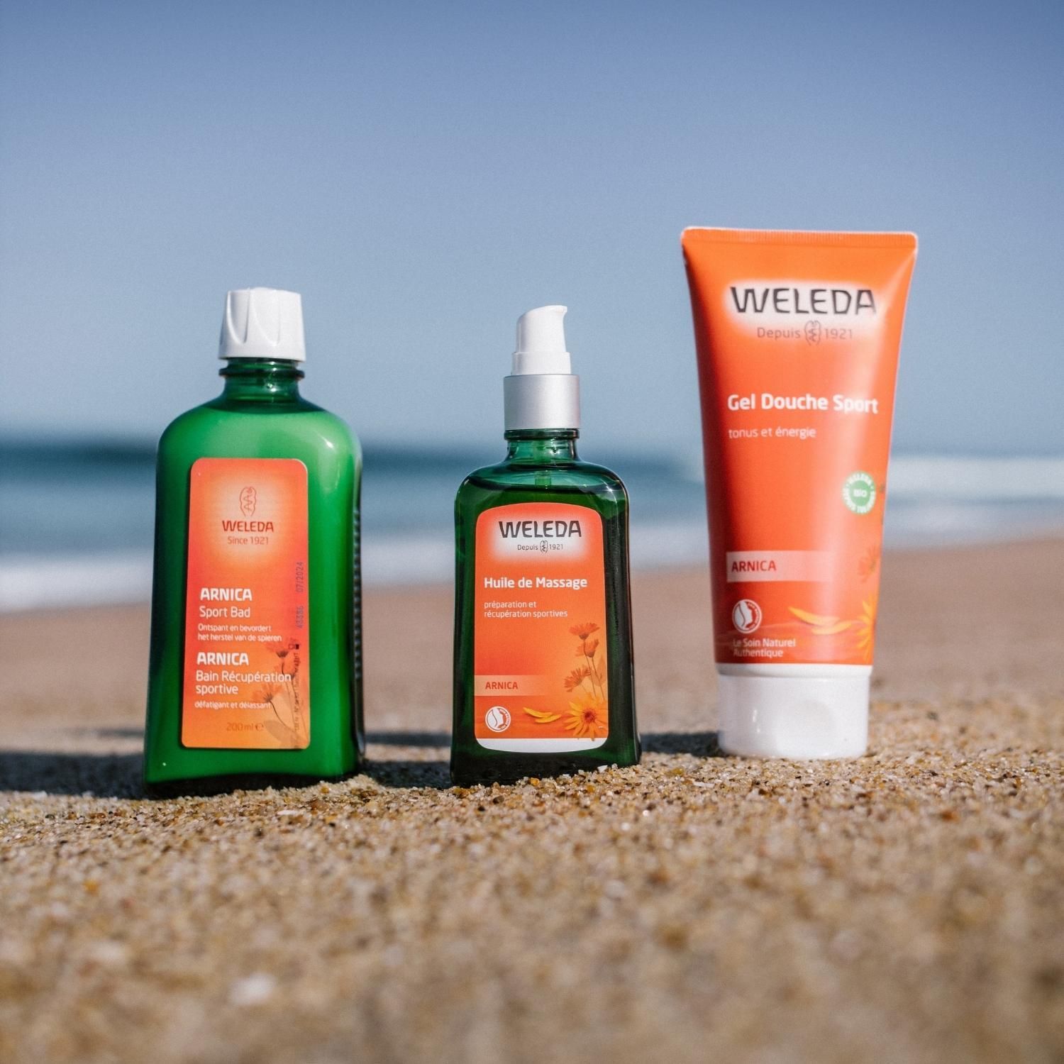 Trois produits Weleda sur la plage. Flacon, vaporisateur et tube. Tous avec logo.