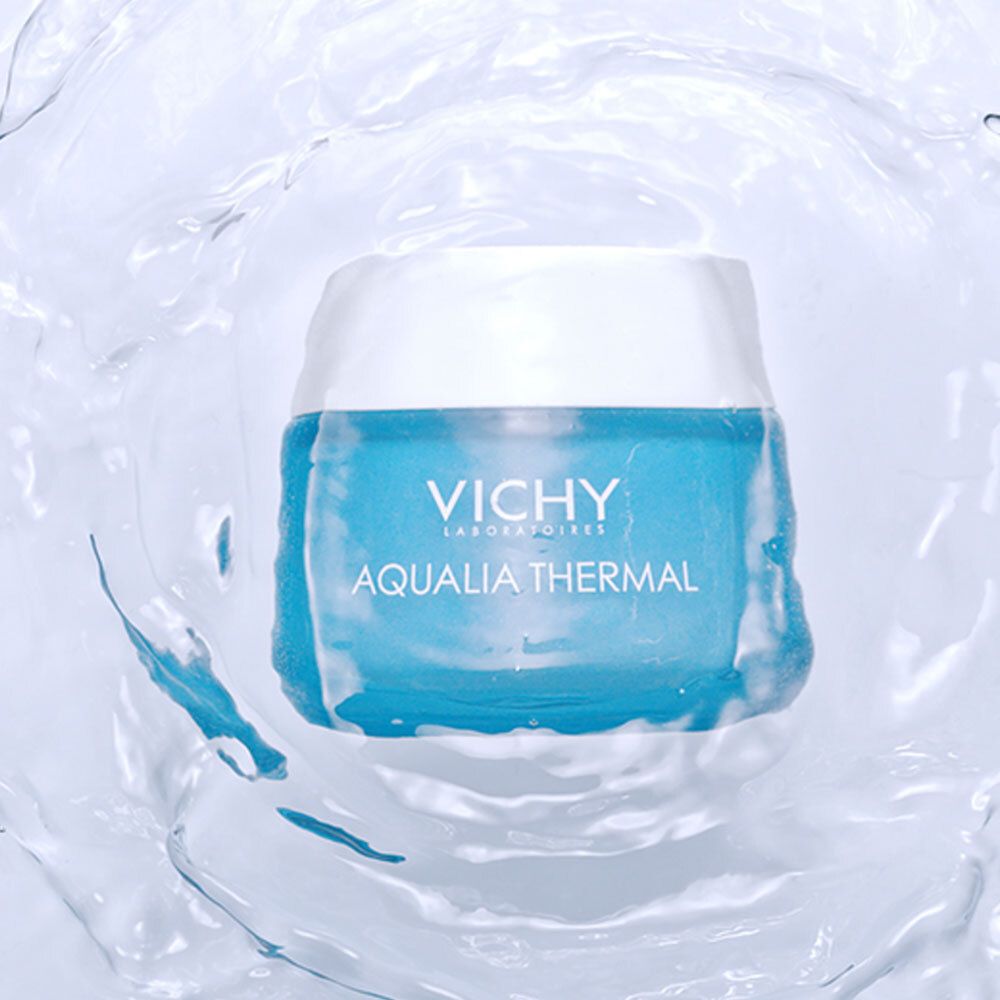 Blaues Cremeglas in Wasser. Aufschrift: VICHY, AQUALIA THERMAL. Wasser spritzt um das Glas.