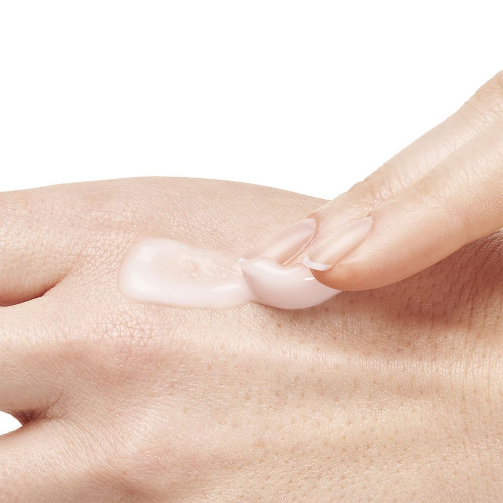 Main avec doigt appliquant de la crème sur la peau. La crème est rose et brillante.