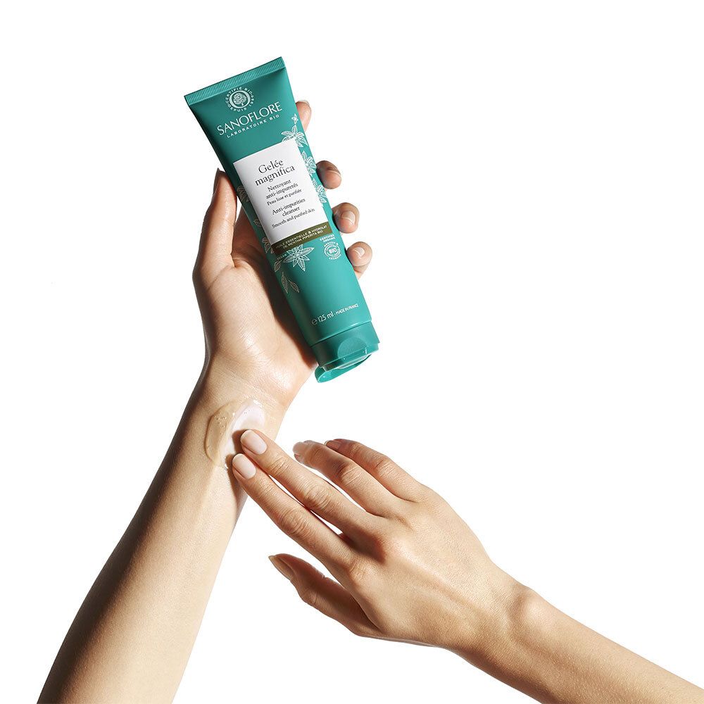 Mains tenant un tube. Produit : Gelée magnifica. Une petite quantité du produit est sur la paume. Fond blanc.