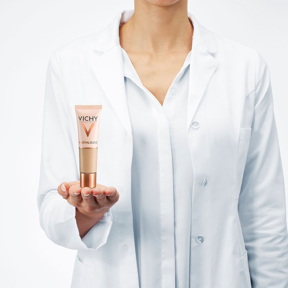Personne tenant le fond de teint VICHY Mineralblend Nr. 09 Achat. La personne porte une blouse blanche. Produit en main.