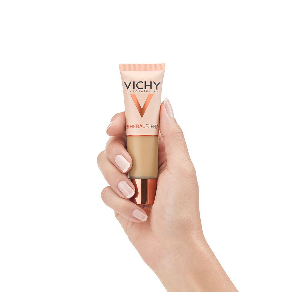 Main tenant le fond de teint VICHY Mineralblend Nr. 09 Achat. Produit en main. Tube rose-doré.
