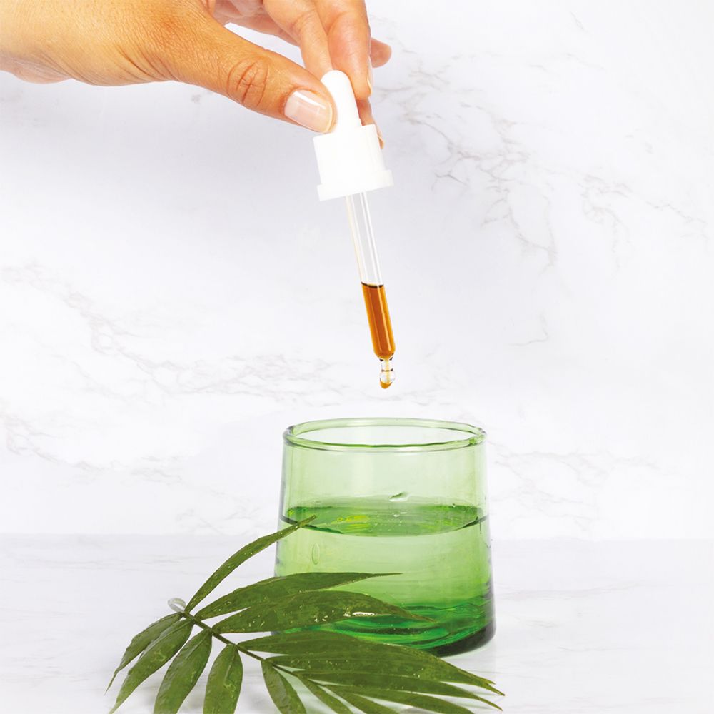 Main avec compte-gouttes au-dessus d'un verre. Gouttes tombant dans un verre avec liquide. Feuille verte.