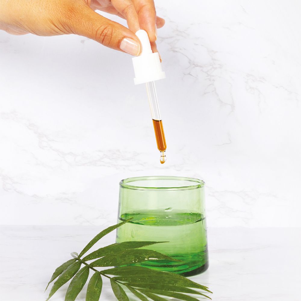 Pipette avec goutte au-dessus d'un verre vert. Liquide qui coule. Fond: marbre. Pas de nom de produit.