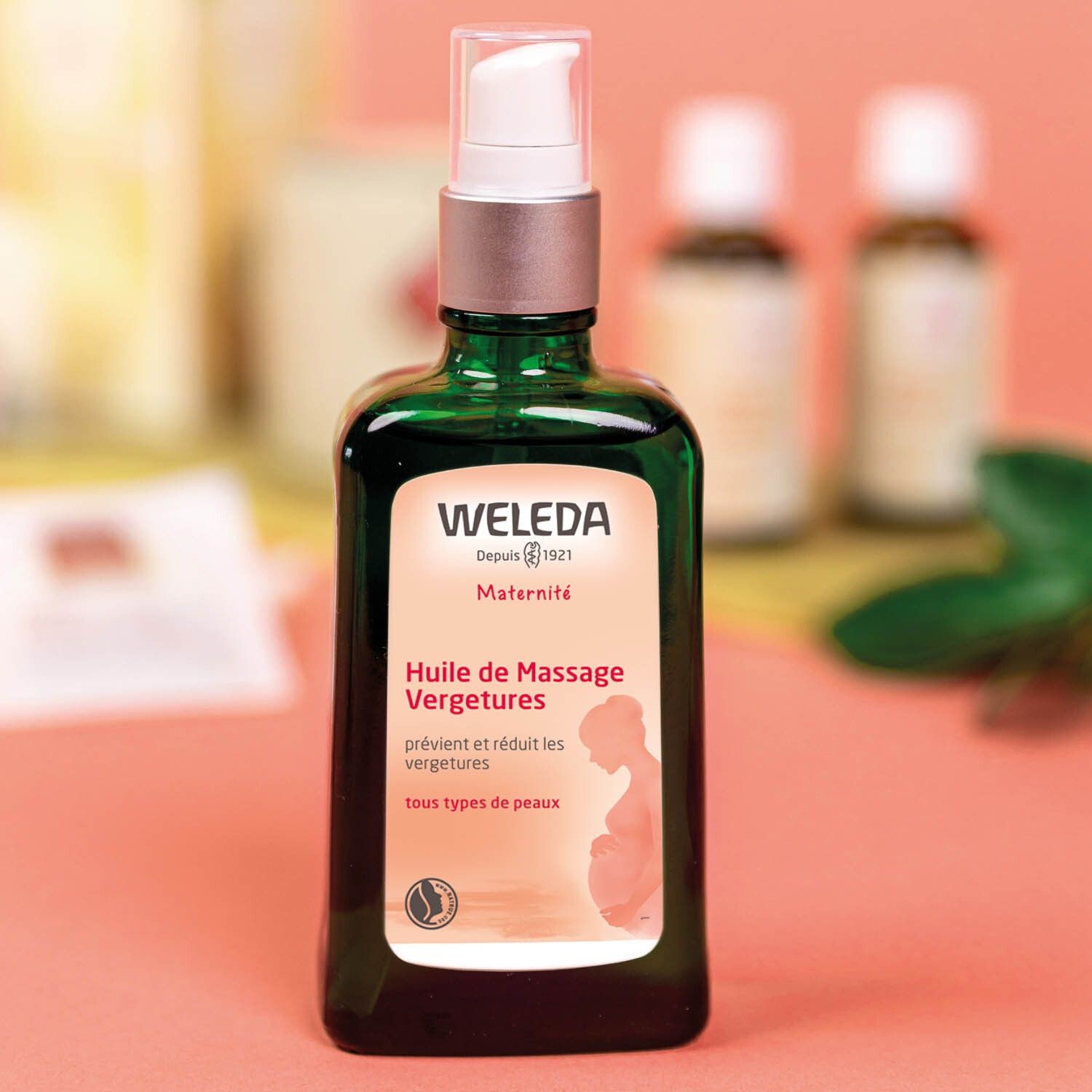 Groene fles WELEDA Massageolie tegen Striae. Tekst: Maternité, voorkomt en vermindert striae. Roze achtergrond.