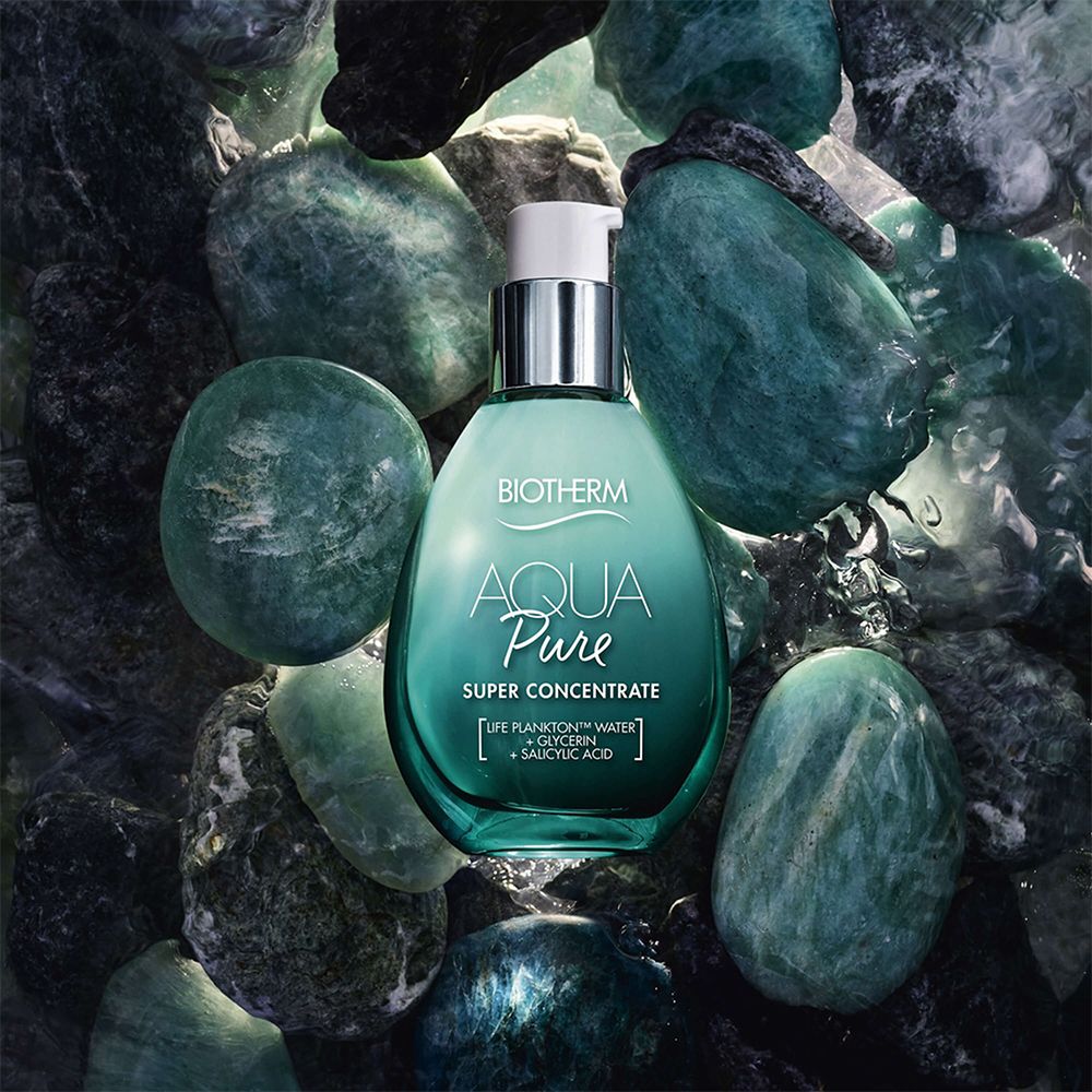 Türkisgrüne Flasche mit Pumpe, umgeben von grünen Steinen. Aufschrift: Biotherm Aqua Pure Super Concentrate.