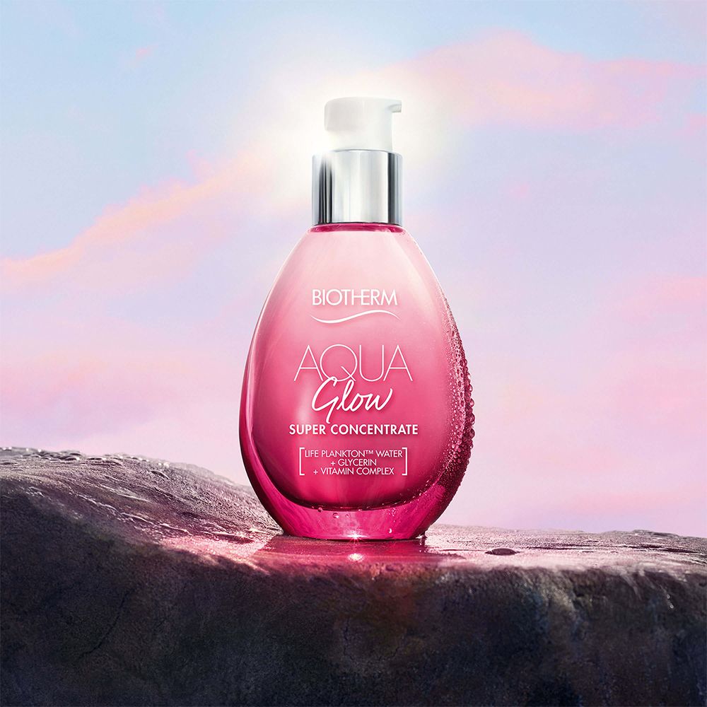Rosa Flasche mit silbernem Pumpkopf auf Felsen. Aufschrift: BIOTHERM AQUA Glow SUPER CONCENTRATE.