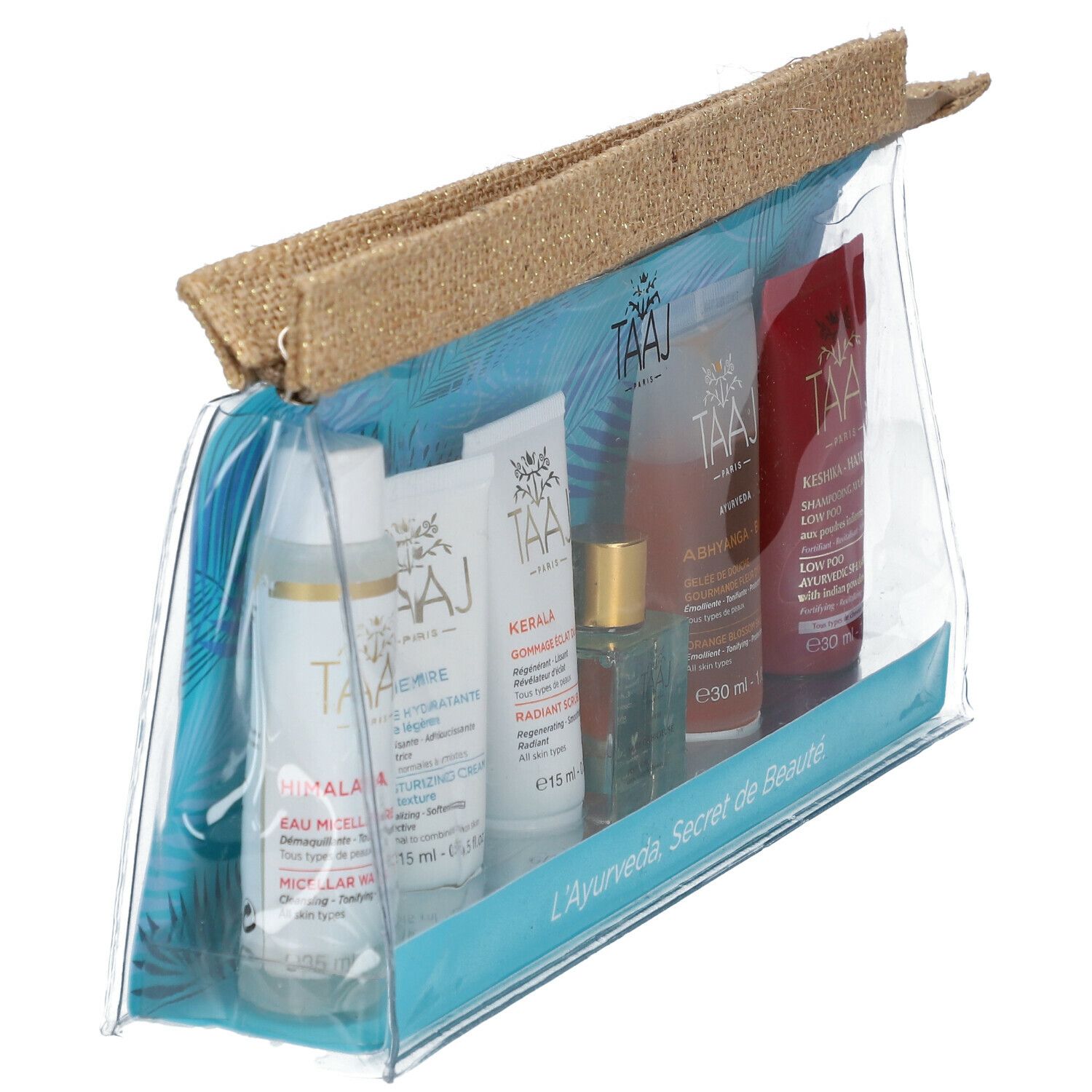 Klare Kosmetiktasche mit sechs Produkten. Aufschrift: TAAJ. Produkte in Flaschen und Tuben. Aufschrift: L'Ayurveda, Secret de Beauté.