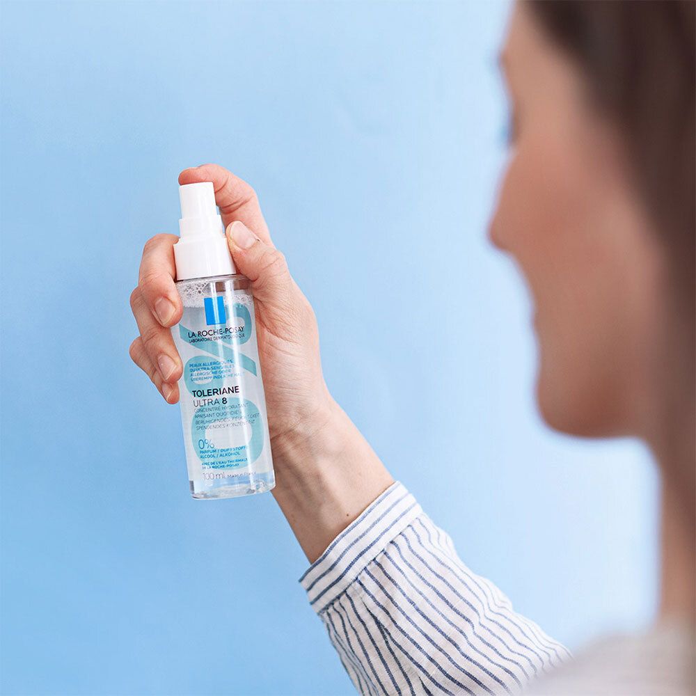 Personne vaporisant avec un flacon spray. Inscriptions: LA ROCHE-POSAY, TOLERIANE ULTRA 8. Fond bleu.