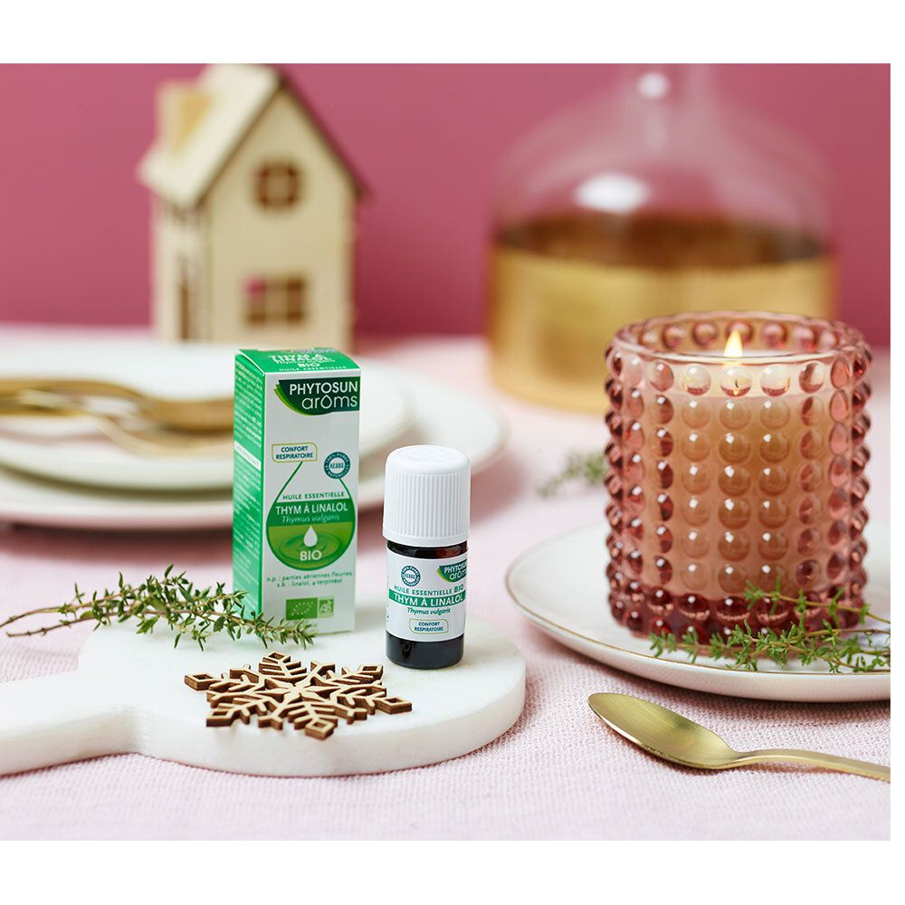 Produktflasche und Schachtel auf einem Tisch, dekoriert mit Kerze, Holzstern und Zweigen.