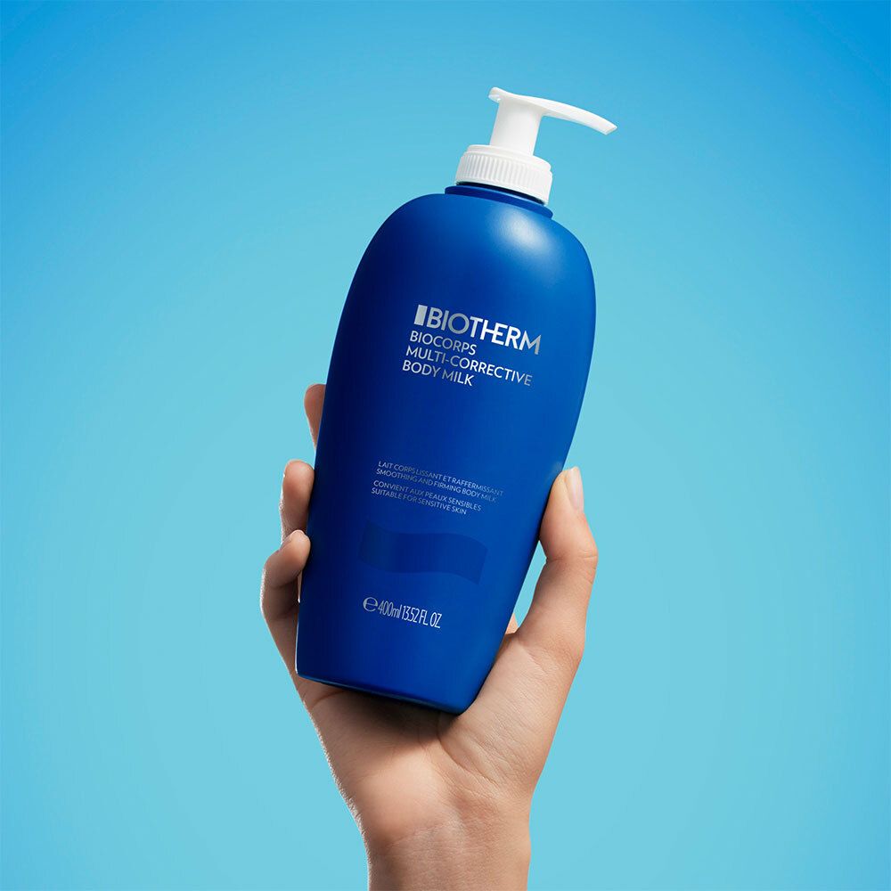 Blaue Flasche mit weißem Pumpverschluss, in einer Hand gehalten. Aufschrift: BIOTHERM, Biocorps Multi-Corrective Body Milk.