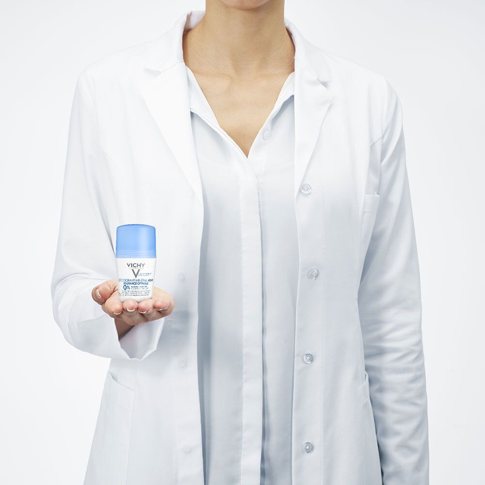 Une personne en blouse blanche tient un déodorant roll-on. Contenant blanc, bouchon bleu.